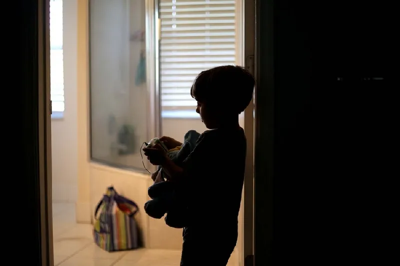 暗い部屋で一人でおもちゃを抱えて遊ぶ子供。自閉症のリスクを連想させる孤独な遊びの様子