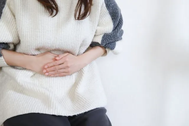 白いセーターの女性が生理痛でお腹を抱える様子を漢方治療で改善