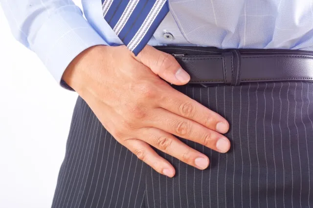 スーツ姿の男性が下腹部を押さえて尿トラブルを表現するイラスト