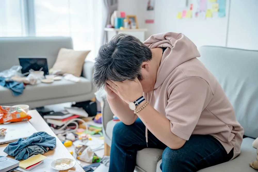 体がだるくて死にそう、両手で額を押さえてソファにぐったり座る50代男性