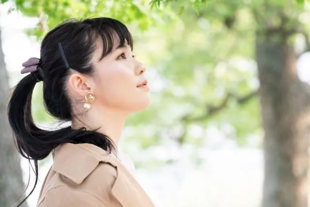 黒髪の若い女性が穏やかな表情で斜め上を眺め、背景に森の木々がぼんやりと広がる様子。精神的な安定を象徴するイメージ。