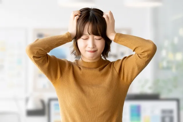 心配事やストレスで頭を抱える女性（黄色いセーター）