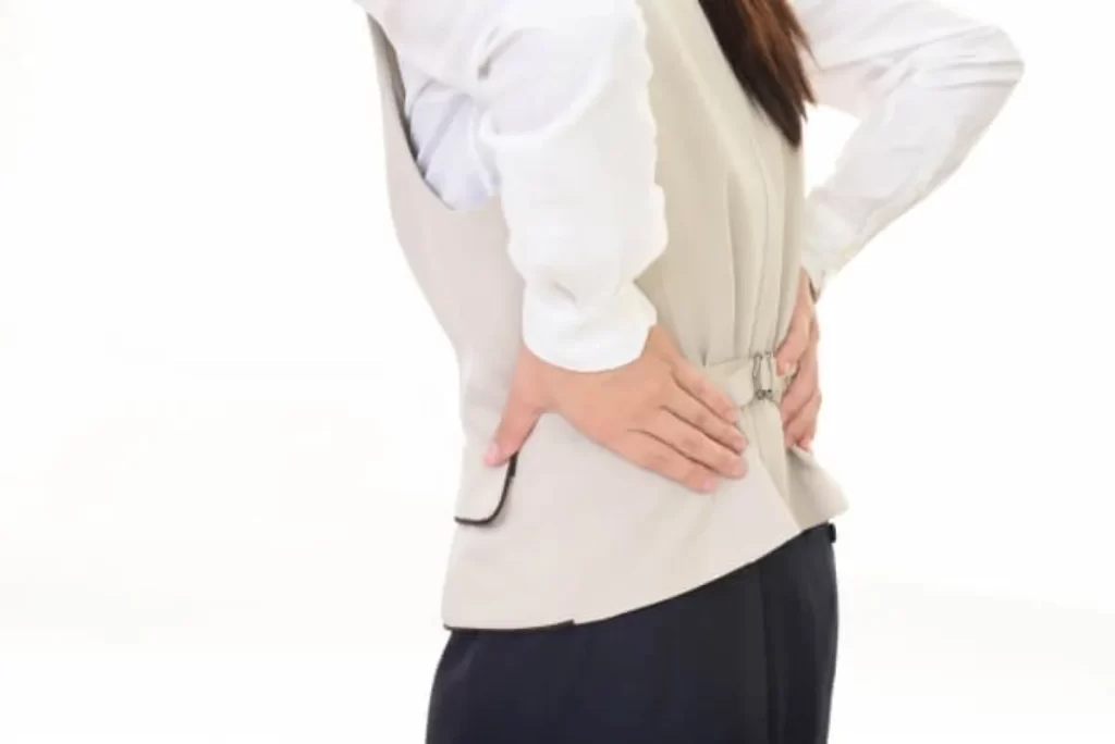 薬剤師が両手で腰を抑えている様子。激しい腰痛で歩行が困難になった状態を表す