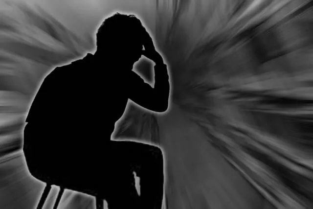 逆光の中、椅子に座って頭を押さえる男性のシルエット
