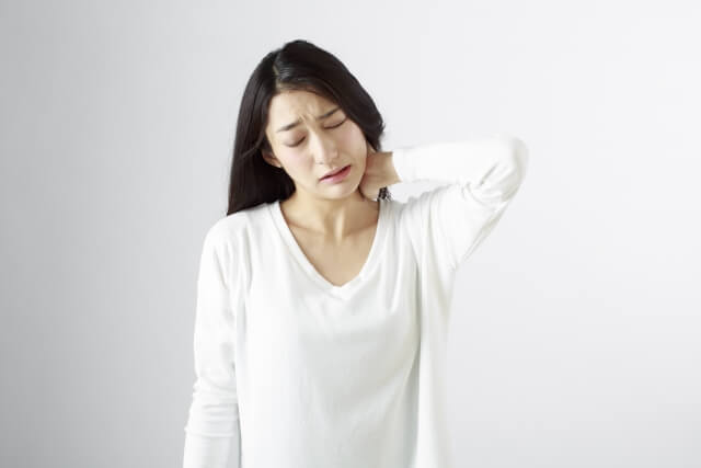 白い服を着た女性が左首の痛みを訴えて首を触っている様子