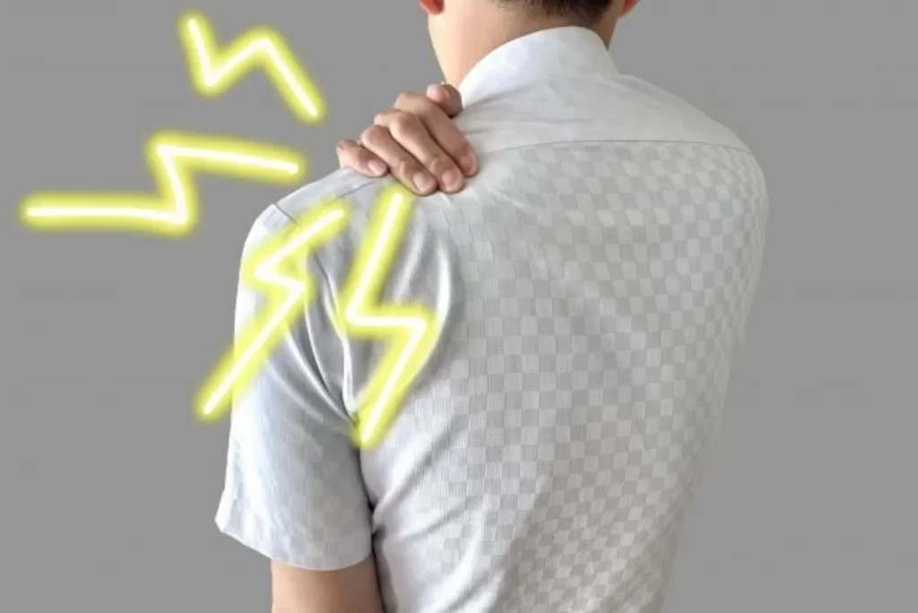 雨が降る前に悪化する肩の関節痛で、左手で左肩を押さえる男性の後ろ姿（チェック柄シャツ）