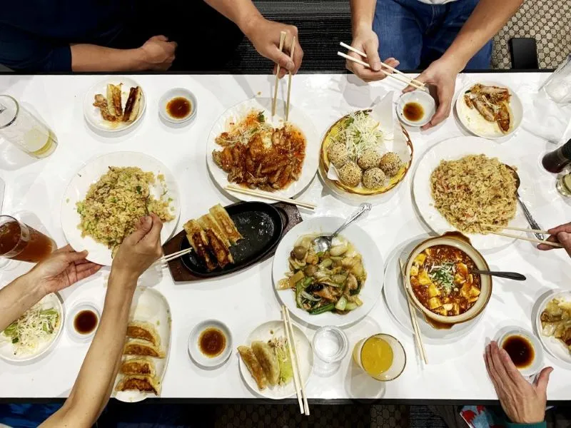大勢の人が中華料理を囲み、箸を伸ばして食事を楽しむ俯瞰の光景