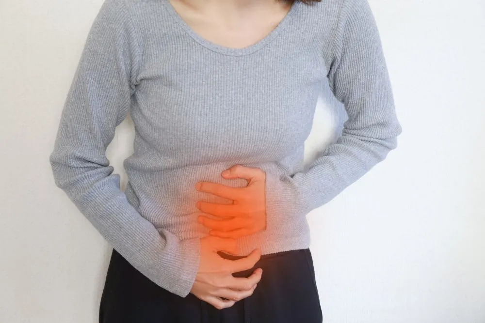 鉄剤の副作用による胃痛を訴える女性。お腹部分を赤くハイライトして痛みを表現した画像。