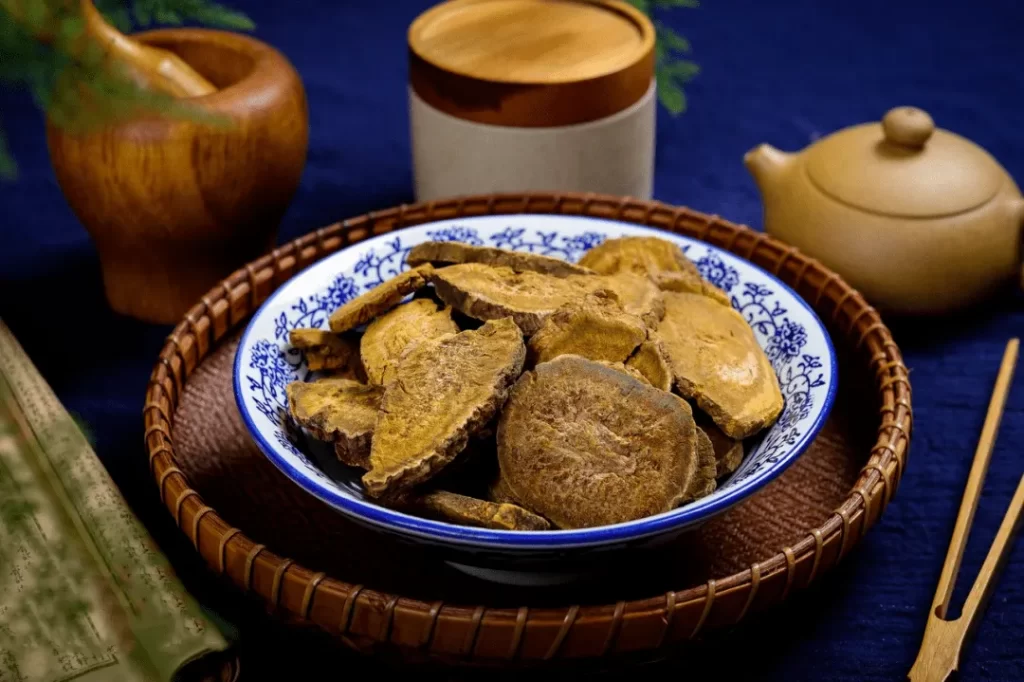 中国風の藤ザルと青い皿に盛られた生薬の大黄、医書と薬壺が並ぶ写真