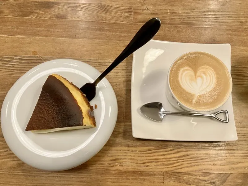 白い皿のバスクチーズケーキとカフェラテの俯瞰画像 その他の行を表示する