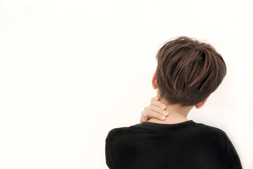 首の痛みに苦しむ男性の後ろ姿。黒い半袖シャツを着て、頚椎部分を触って不快感を示している。