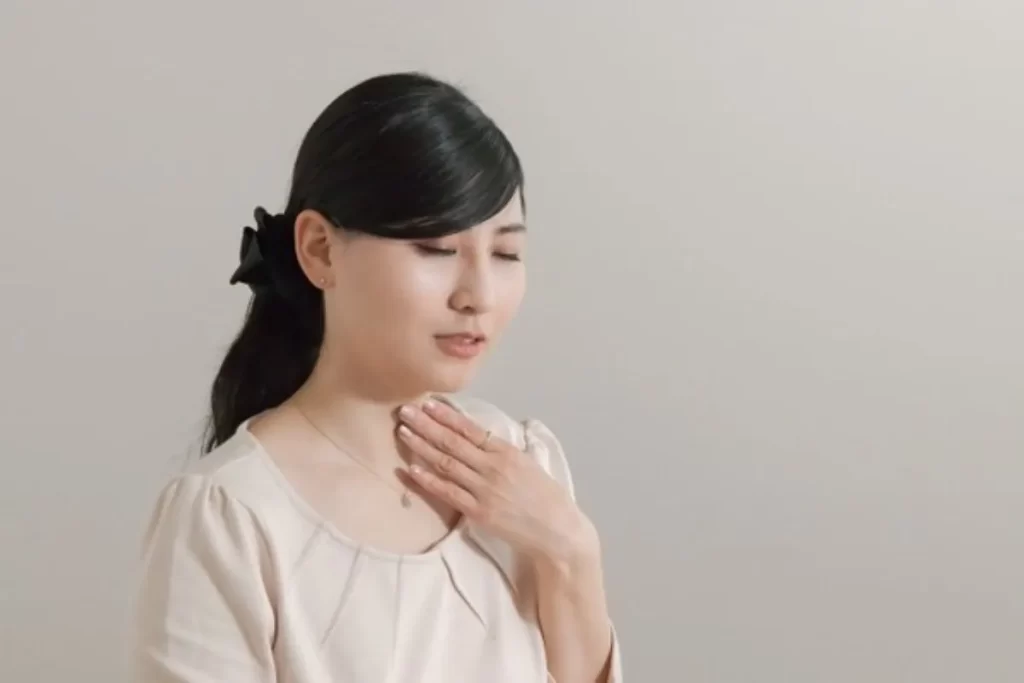 風邪の初期症状で喉が痛い女性が左手で喉を押さえている様子