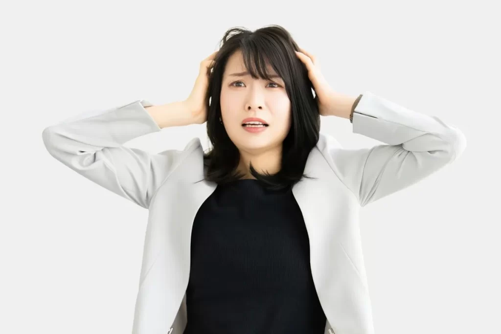 頭を抱えて困った表情をしている白いジャケットのビジネスウーマン