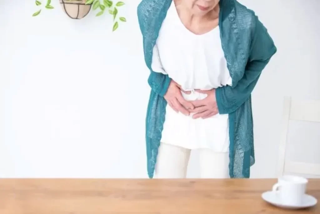 急な腹痛で前かがみになり、お腹を両手で抱えるシニア女性。食積による激痛のイメージ。