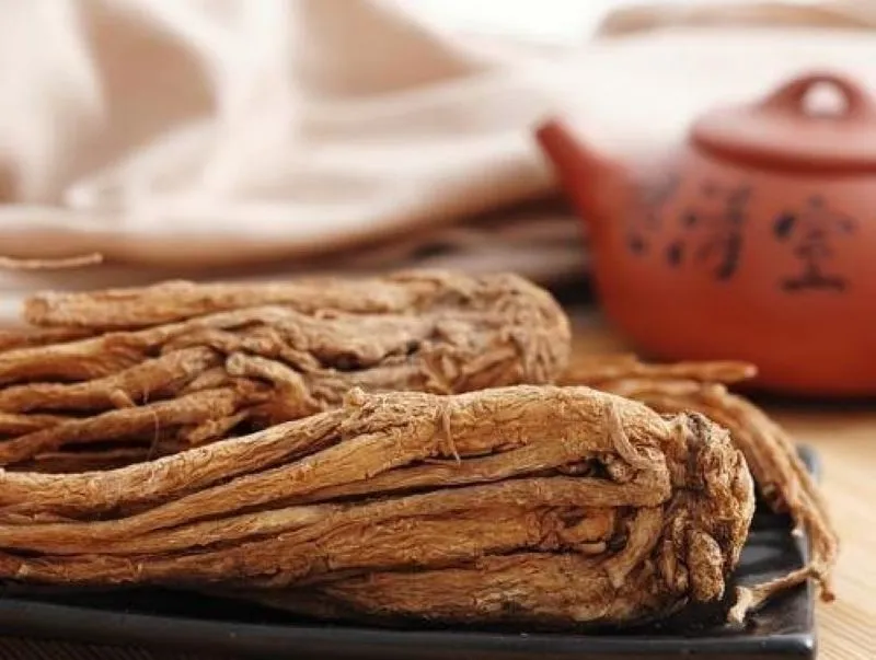 黒い陶器皿に横たえられた当帰と、背景に見える薬草を煎じるきゅうす