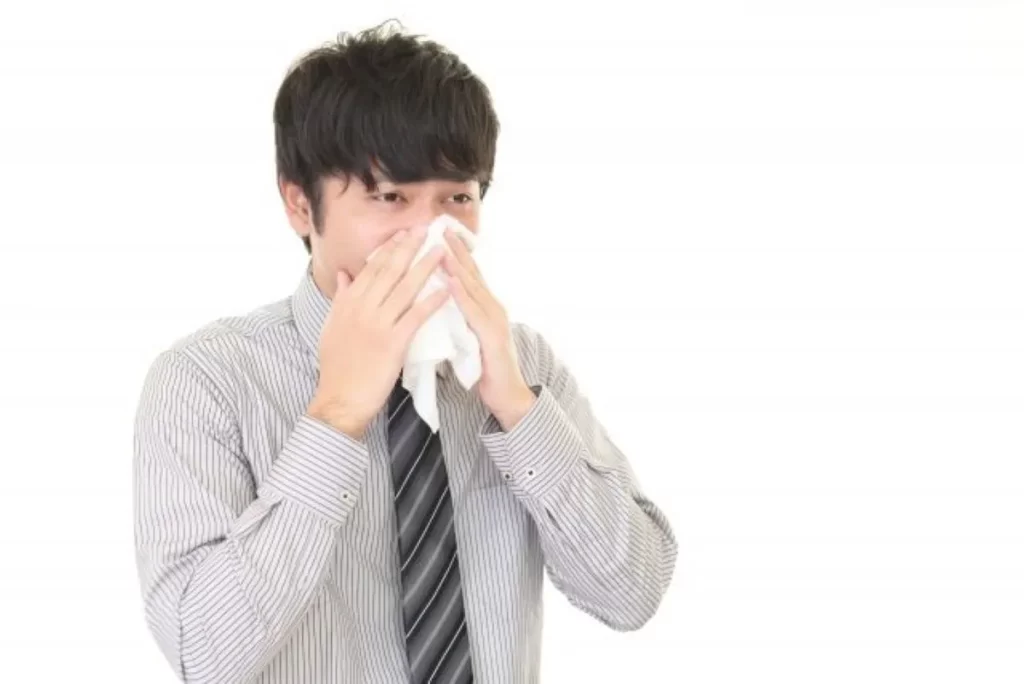 鼻水が止まらずティッシュで鼻をかむスーツ姿の男性。風邪による透明な鼻水のイメージ
