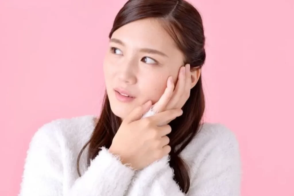 左ほっぺを押さえて歯茎の痛みに悩む白いセーターの女性の写真