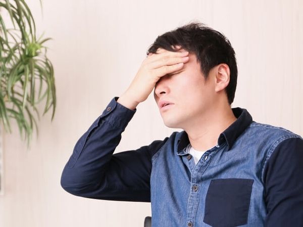 慢性白血病による低熱でつらそうに頭を触る男性
