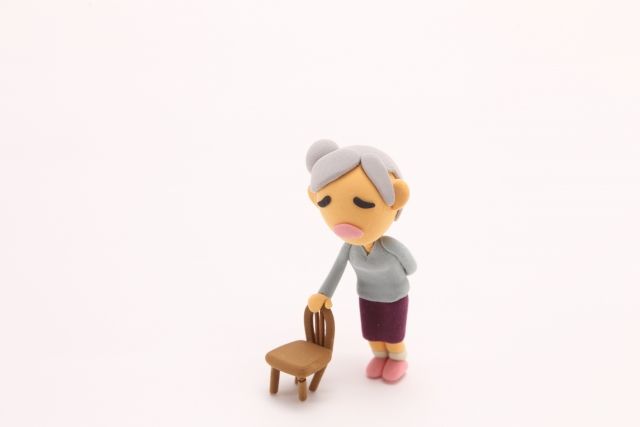 腰痛とお尻から太もものしびれに悩むシニア女性が椅子に手を置いて立っている様子