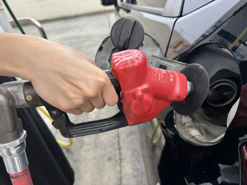 ガソリンスタンドで静電気を気にして給油する女性の手、火災防止の注意喚起