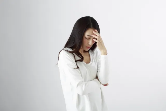 頭痛でおでこを押さえる女性（鍼治療前の痛みイメージ）