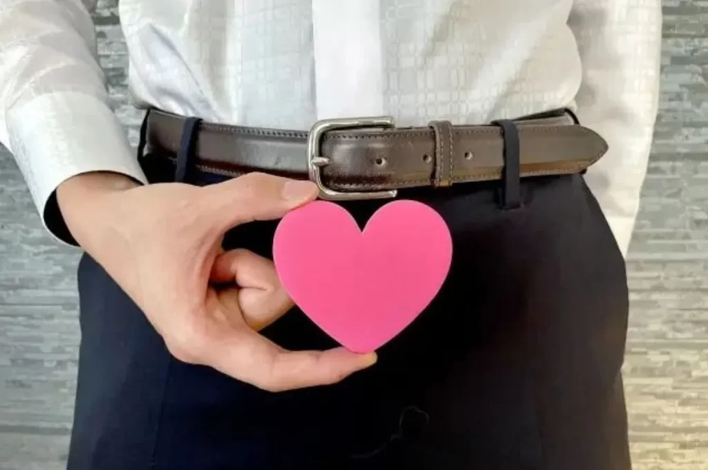 スーツ姿の男性がベルト前にピンクのハートを持ち、男性不妊やEDの悩みを象徴している様子