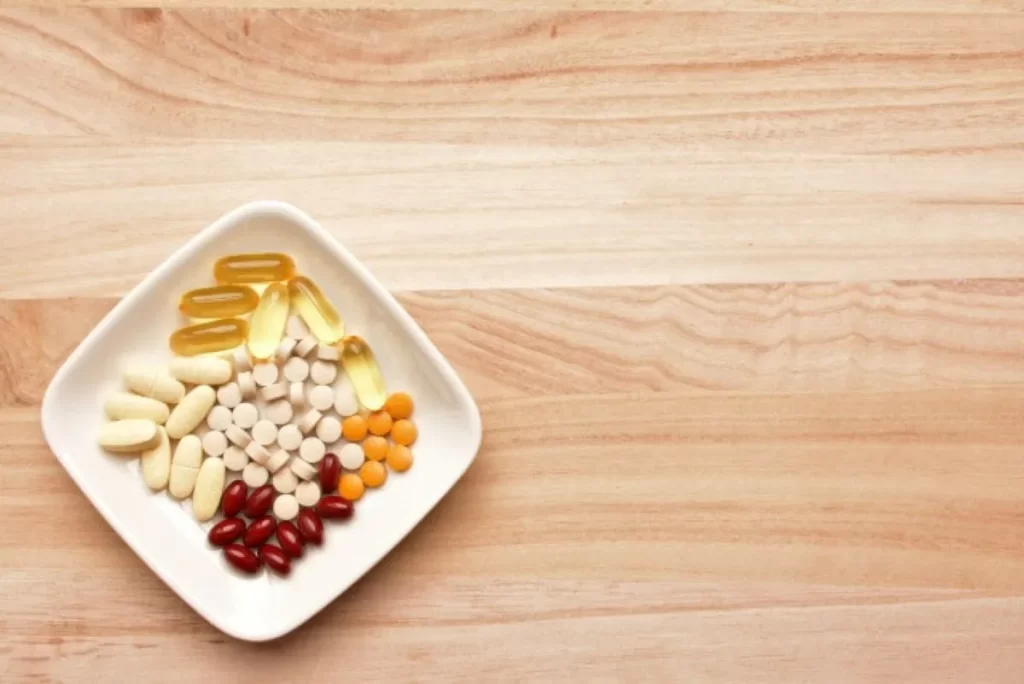 木製テーブルに置かれた四角い容器に入った複数のサプリメント。妊活目的で飲む亜鉛サプリが皮膚に発疹を引き起こす可能性を示す画像。