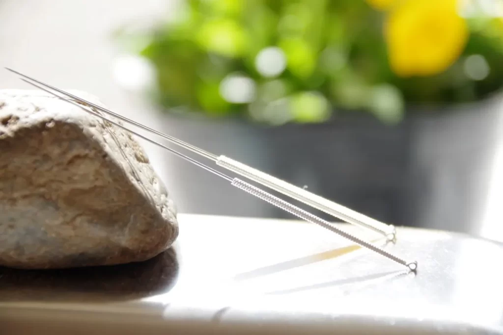 石に斜めに置かれた数本の鍼と黄色い花の背景を持つアイキャッチ画像。鍼治療で健康な尿の色を取り戻すテーマを表現。