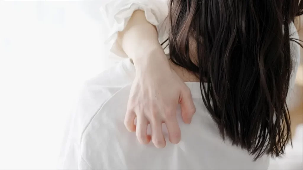 背中のムズムズ感が気になり左背中を掻く女性