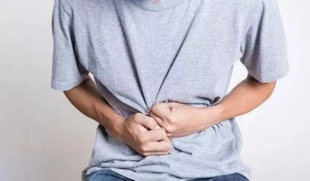 胃のあたりを両手で強く押さえて痛みをこらえる男性のクローズアップ