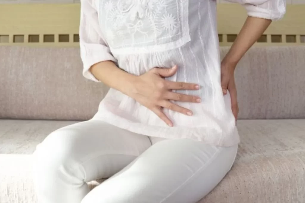 お腹の冷えと腰の冷えに悩み、ソファーに座って腹部と腰を押さえる女性
