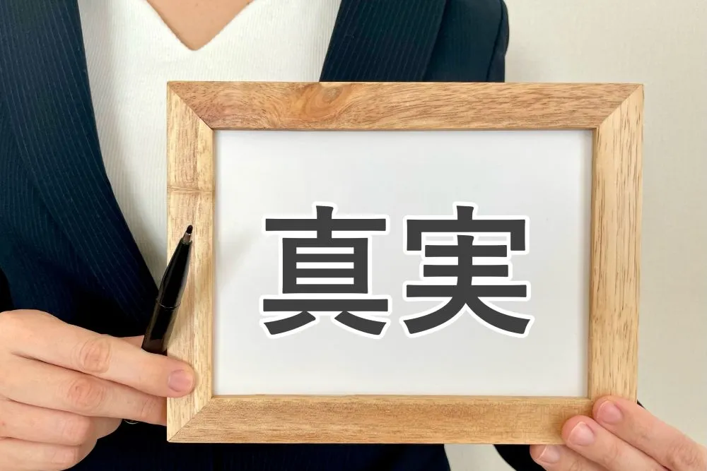 スーツ姿の女性が木製の小さな看板を持っており、看板に「真実」の文字が書かれている画像