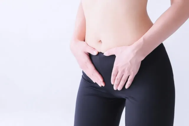 ヨガウェアの女性が鼠径部（足の付け根）を両手で触っているクローズアップ画像。リンパ節の腫れをイメージ。