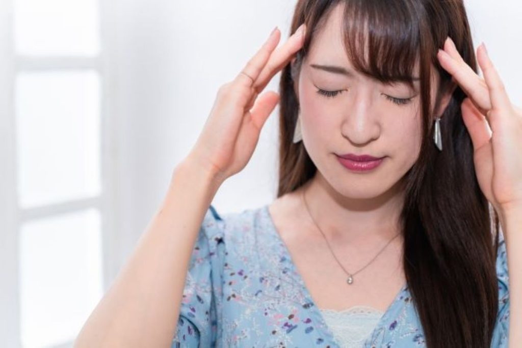 不正出血による重度の貧血でめまいと頭痛に苦しむ女性、太陽穴を押さえて目を閉じている様子