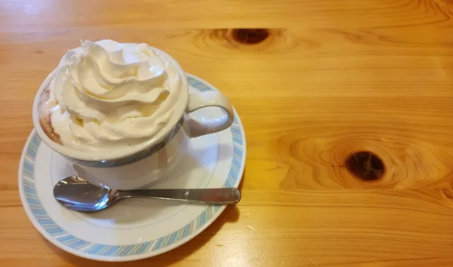 木製テーブルに置かれたコーヒーカップとウインナー。在宅勤務中のコーヒー摂取をイメージ。