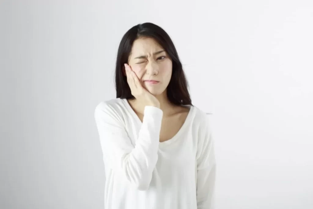 右ほほの痛みで顔をゆがめる女性が頬を押さえている様子