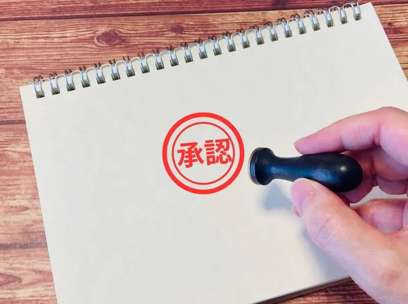 白い紙に押された承認スタンプ。生理不順がワクチン接種後の報告事例として認識されていることを表現したイメージ。