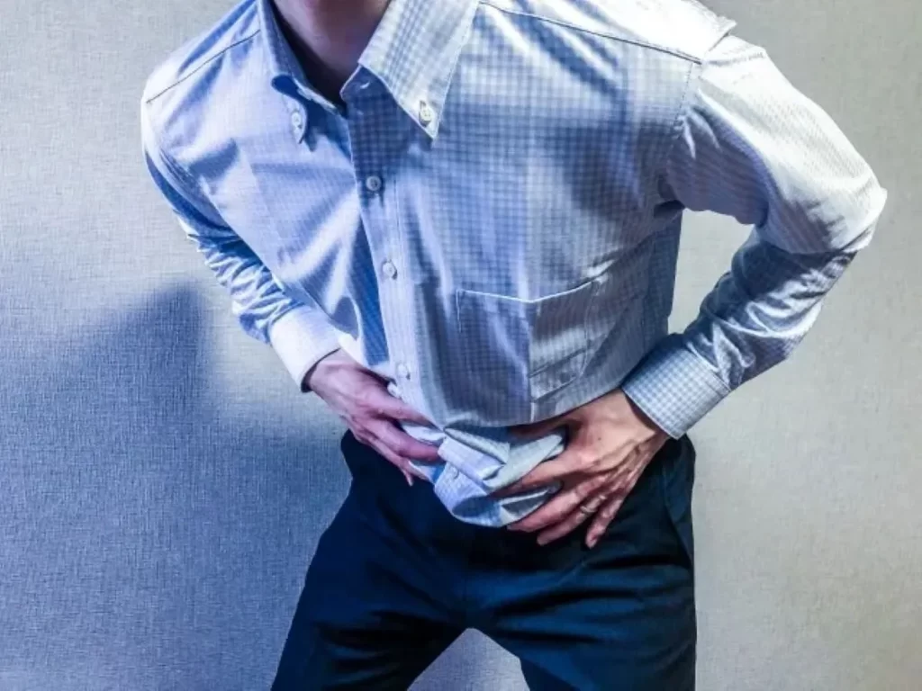 冷えによる腹痛と下痢で前かがみになり、お腹を両手で押さえる男性の様子