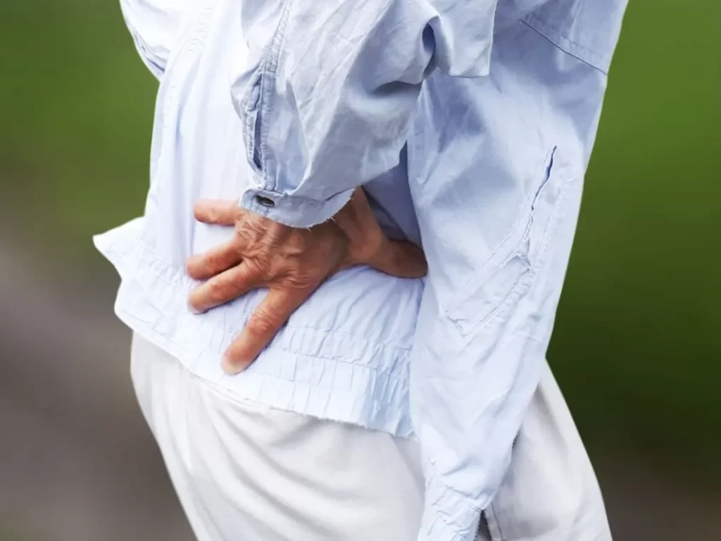 腰の痛みで両手を腰に当てる高齢男性