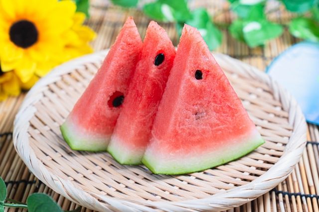 木のザルに盛られた三つのカットスイカと夏の緑の背景