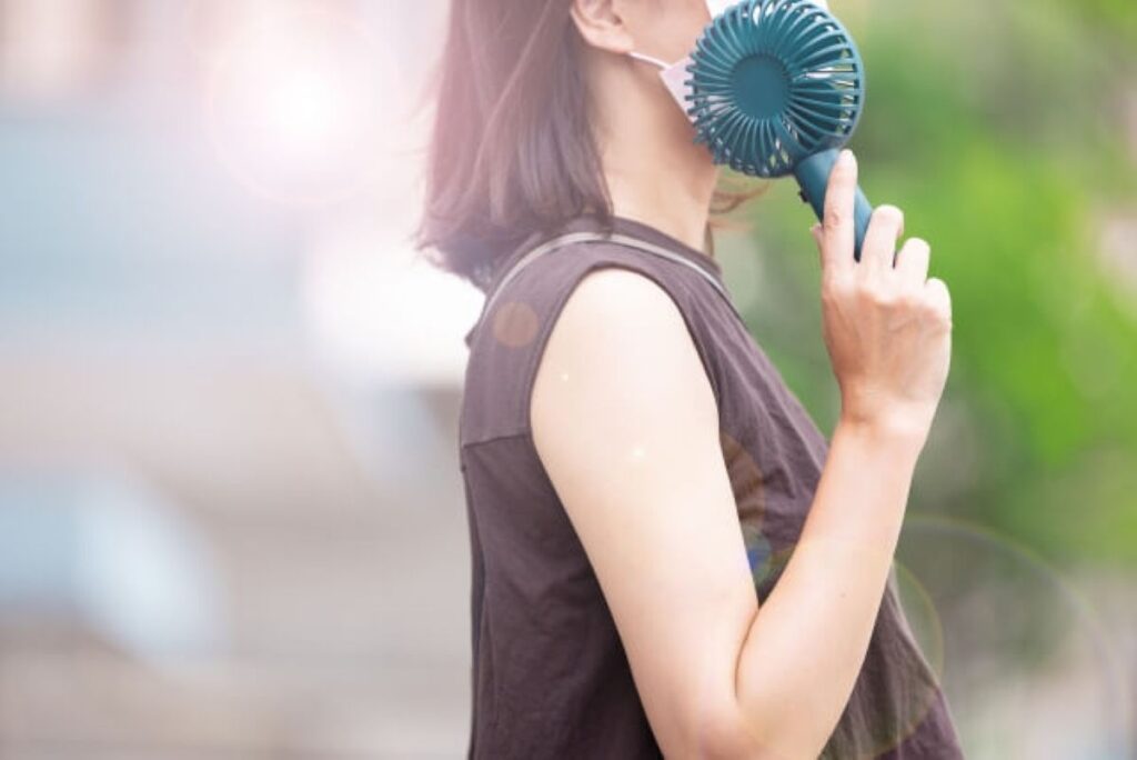 真夏の暑さで小型扇風機を顔に当てて涼む女性のクローズアップ