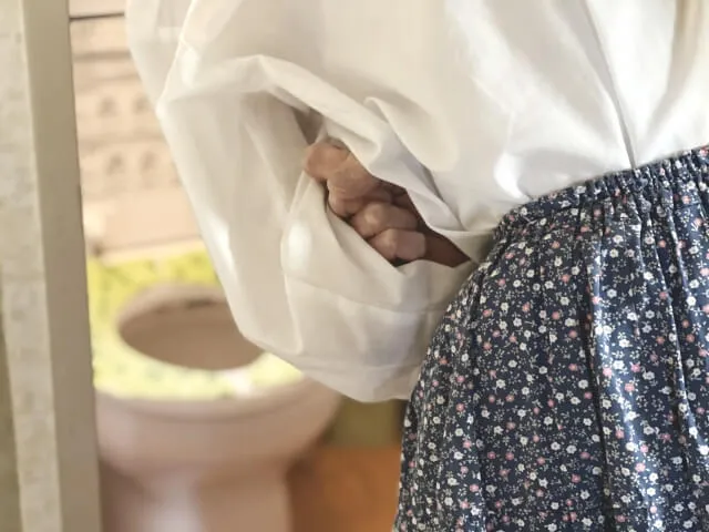 白い長袖のトップスと水玉模様のスカートを着た女性が、便秘による不快感からお腹を抱えている様子。漢方薬で便秘を改善した症例を紹介する記事のアイキャッチ画像。
