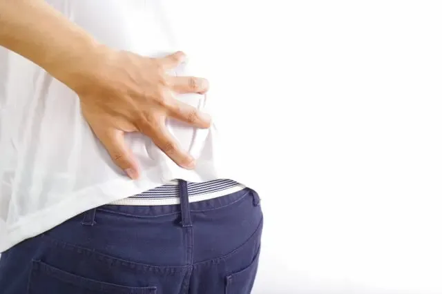 ぎっくり腰で左手で腰を押さえて痛がる、白い半袖シャツと紺色ズボンの男性