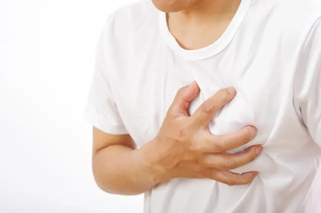 白い半袖を着た男性が右手で胸を強く押さえ、心臓の痛みを訴える様子を表すイラスト。心筋梗塞の症状を象徴。