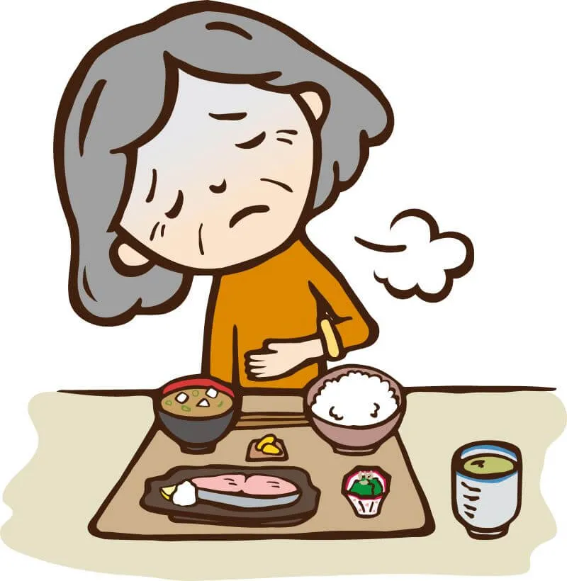 眼の前に料理が置かれているのに、お腹を触りながら苦痛の表情で目を瞑っている高齢女性の漫画風イラスト（食欲不振の症状を表す）