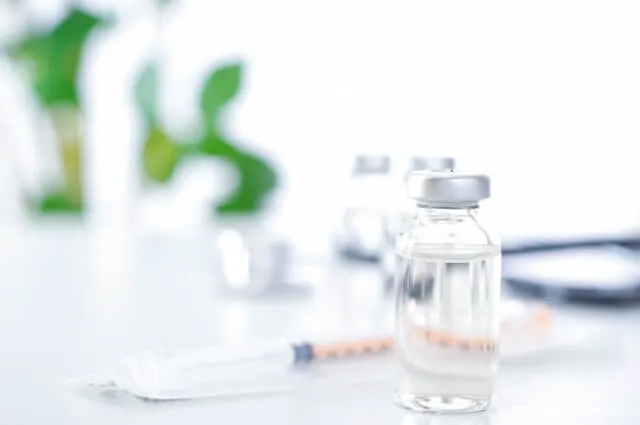 ぼやけた背景に透明な抗がん剤の薬瓶と注射器が並び、緑の葉がうっすら見えるイメージ。抗がん剤の副作用を漢方薬で和らげる治療の象徴。