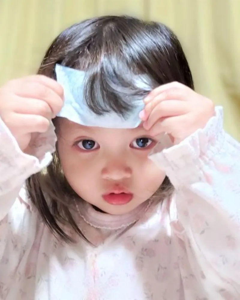 2歳の女の子が熱さまシートをおでこに貼ろうとしている様子。子供の発熱時のケアを表す画像。