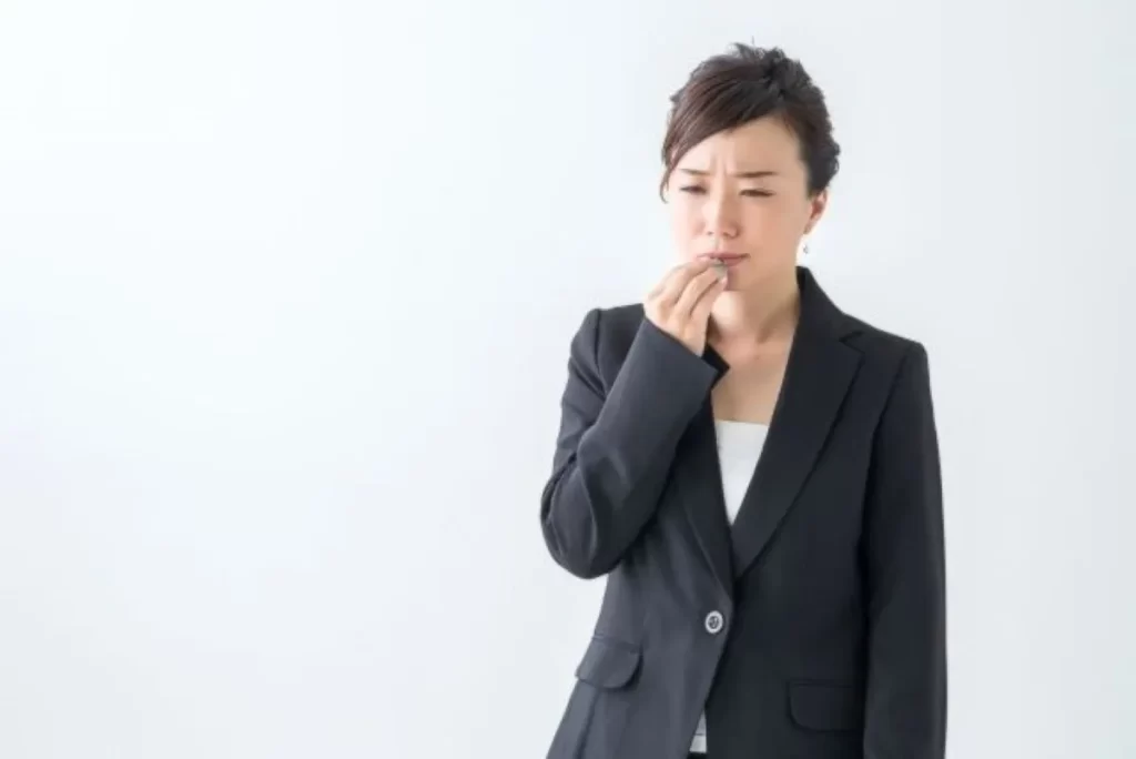 唇のヘルペスの痛みで口元を押さえるスーツ姿の女性