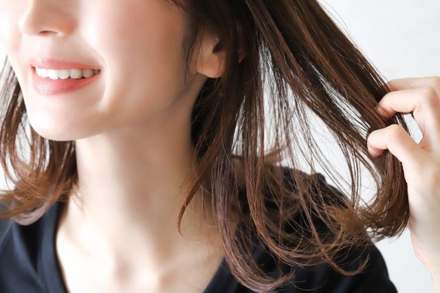髪を触りながら笑う女性が鍼治療で髪ツヤツヤを維持できたことを表現