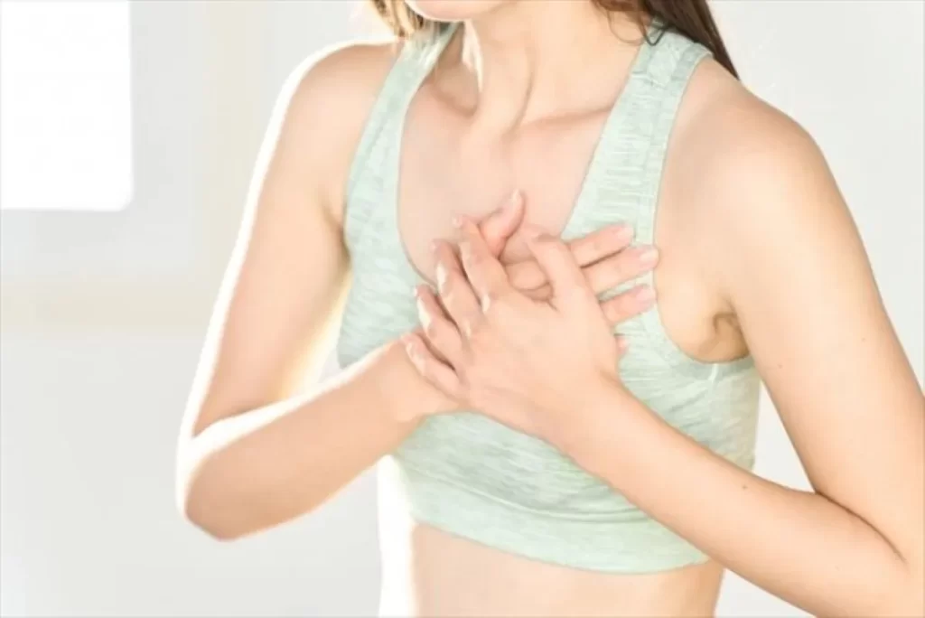 薄い緑色のタンクトップの女性が胸を押さえて不安そうにしている。心臓の不調を示すイメージ。